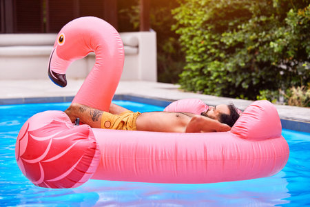 Man, relax and flamingo in swimming pool on vacation for tropical escape, sunshine and chill mode for sunbathing. Male person, floating and summer holiday for leisure, weekend trip and outdoor.の写真素材