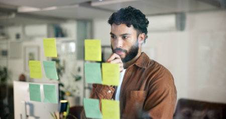 Man, thinking and ideas by glass board for project strategy, planning and sticky note for agenda. Business schedule, brainstorming and storyboard with information, vision and research for inspirationの写真素材