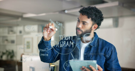 Business, glass wall and man in office, tablet and writing with project, planning and profit growth. Person, employee and consultant in workplace, technology and problem solving with decision or appの写真素材
