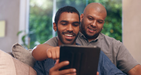 Gay couple, men and smile on sofa with tablet for social media, internet streaming or bonding. Lgbtq, home living room and technology for online app, meme or website conversation with readingの写真素材