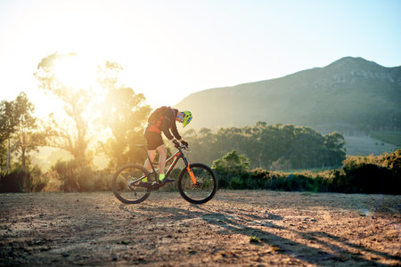 Bike, sport and sunset with man in mountains for outdoor adrenaline, adventure or training. Exercise, fitness or sports and person cycling off road in nature for challenge, competition or performanceの写真素材