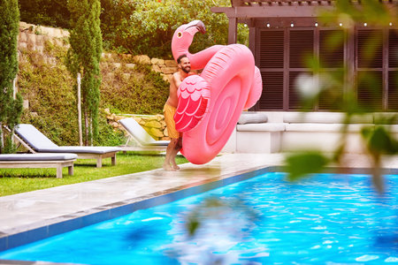 Man, flamingo and fun at pool on holiday, luxury and enjoy the summer at resort. Pink float,...