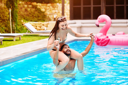 Smile, man and woman on shoulders in swimming pool outdoor with love, support and bonding in water for romance. Happy, couple and piggyback for trust, care and airplane game of freedom on holidayの写真素材