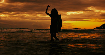 Silhouette, sign and person with surfboard, beach and journey for surfer on holiday, sunset and sea. Ocean, adventure and woman with gesture for fitness, hobby and sports in nature on summer vacationの写真素材