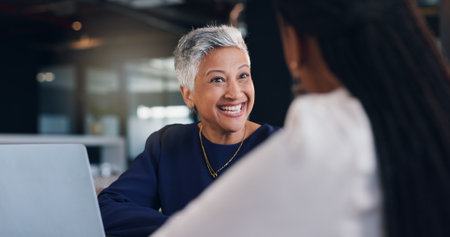 Mature woman, business and happiness with team discussion, positive feedback or investment for project. Conversation, communication and collaboration with laptop for online review or funding approvalの写真素材