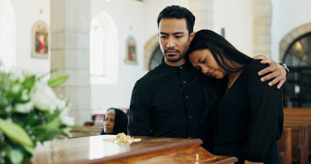 Death, comfort or couple mourning at funeral in church for respect, support or embrace for loss together by coffin. Sad man, woman or grief at memorial service with casket for goodbye, rip or consoleの写真素材