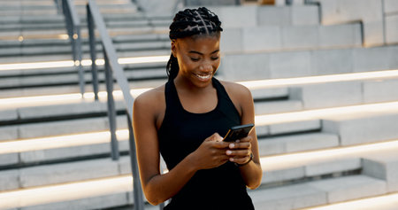 Runner, phone and smile with black woman in city for fitness app, tracking progress and health. Wellness, training and speed challenge with person and mobile for exercise, sports and cardio guideの写真素材