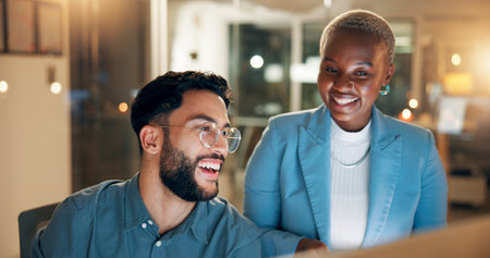 Computer, laughing and night with business people in office together for development or planning. Feedback, funny or review with employee man and woman at work for project management in eveningの写真素材