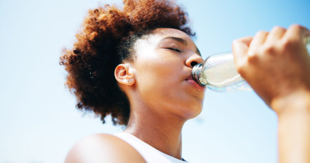 Woman, runner and drinking water with fitness, outdoor and break for hydration, detox and low angle....
