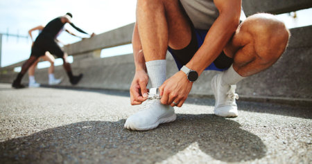 Fitness, hands and tie shoes on street to start workout, training and exercise for practice on road. City, man and runner tying laces on sneakers for sports, preparation and ready for challengeの写真素材