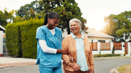 Senior, woman and walking with nurse outdoor with laughing, funny conversation and retirement wellness. Happy, caregiver and old person in road with mobility support, bonding together and fresh airの写真素材