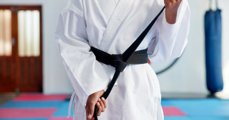 Hands, black belt and person in karate dojo for self defense training, skill level or martial arts. Ready, student and prepare for fight, tying knot for experience and taekwondo with growth or sportsの写真素材