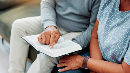 Hands, senior couple and bible reading on sofa for religious study, spiritual praise or faith in Jesus Christ. Old people, worship or holy gospel in home for scripture meditation, prayer or knowledgeの写真素材