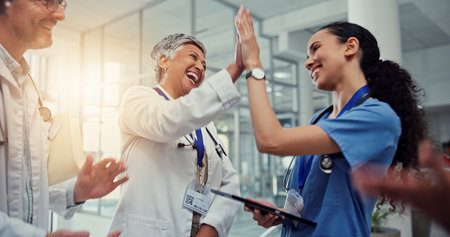 Nurse, doctor and celebration high five with tablet for healthcare excellence, surgery success and good news. Medicine staff, people and happy at hospital for medical results and achievement supportの写真素材