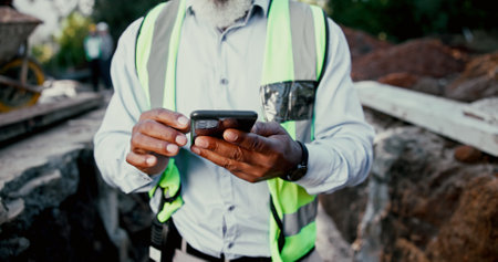Construction site, hands and phone with person outdoor for communication, excavation or update. App, building and contact with professional developer typing on mobile for architecture or planningの写真素材