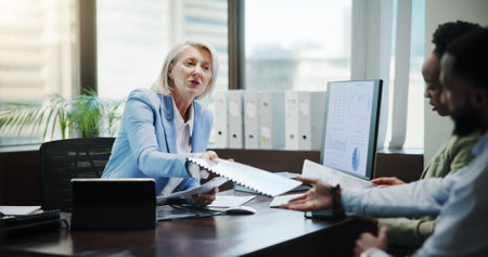Woman, documents and business people for finance at office, review or feedback with charts by computer. Mature mentor, accounting and discussion with team, inspection and planning at corporate agencyの写真素材