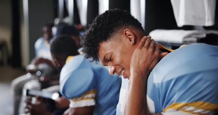 Man, football player and neck pain with injury in locker room, frustrated or sprain with American sport. Person, muscle ache and athlete team with strain, bruise or massage for inflammation at clubの写真素材