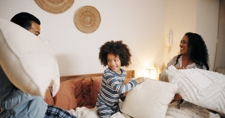 Happy family, bedroom or playing with pillow fight for fun bonding, game or holiday together at home. Dad, mom and playful child enjoying weekend, activity or cushion war with pajamas in bed at houseの写真素材