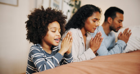 Family, bed and praying with hands together for faith, christianity religion or belief on fabric sheets at home. Mom, dad and child with hope or gratitude for god, holy routine or worship in bedroomの写真素材