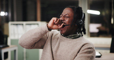 Agent, tired or black man yawning in call center overwhelmed by telecom deadline, burnout or overtime. Headset, night or overworked consultant with fatigue, double shift and telemarketing serviceの写真素材