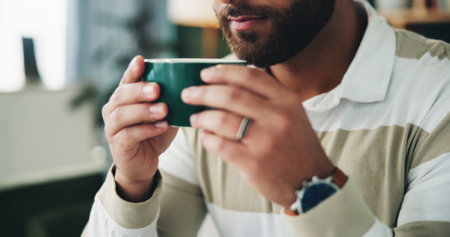 Home, man and hands with coffee to drink, warm beverage and espresso in living room on weekend. House, male person and relax with aroma smell for matcha, tea cup and comfortable on couch in loungeの写真素材