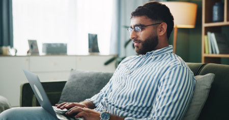 Home, man and typing on laptop for remote work, online information and story for publication. Sofa, freelancer and male content writer with tech for research, copywriting and article website in houseの写真素材