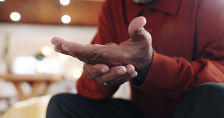 Mature man, hand pain and arthritis on couch in home, carpal tunnel and joint problem with gout. Palm, senior person and bone inflammation with rheumatism, crisis and living room with strain injuryの写真素材