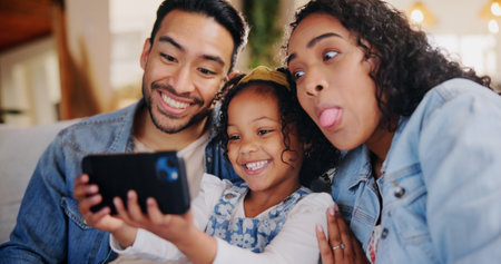 Parents, happy and laugh with selfie on sofa, playful and bonding with post on web in family home. People, mother and father with child, photography and comic joke with love in living room at houseの写真素材