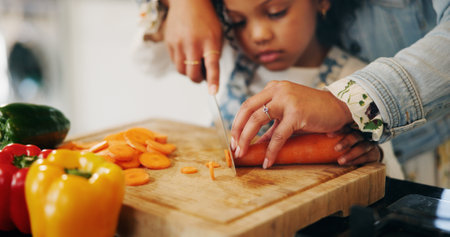 Hands, mother and child with vegetables to chop, cooking and bonding with learning skills at home. Kitchen, girl and mom with teaching for cutting, organic food and meal prep with carrots as familyの写真素材