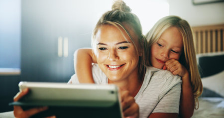 Happy mother, child and relax with tablet on bed for online entertainment, show or cartoon at home. Mom, daughter or kid lying with smile on technology for subscription, app or streaming in bedroomの写真素材