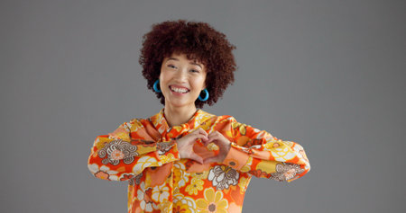 Happy woman, portrait and fashion with heart hands in studio for retro style on a gray background....