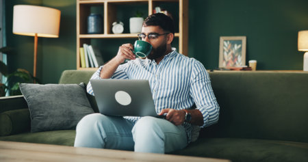 Man, drink and coffee with laptop at house for morning start, research and schedule update of article. Male person, beverage and online information, reading feedback and editing story for publicationの写真素材