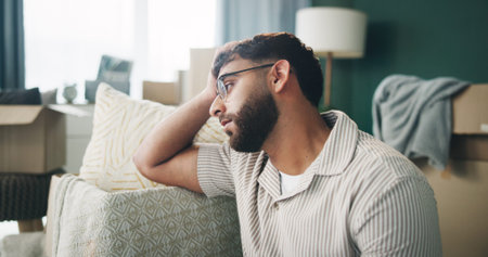 Boxes, depression and thinking with man on sofa in living room of home for mortgage failure or...