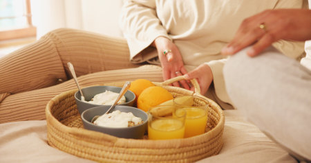 Home, couple and hands in bed for breakfast, nutrition and bonding together on weekend holiday. Closeup, morning and people with food for wellness, healthy diet or porridge with orange juice in houseの写真素材