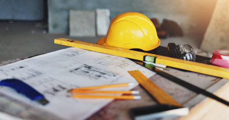 Architecture, blueprint and drawing tools with hard hat for industrial renovation, building design and planning. Safety equipment, scale and floor plan at construction site for project developmentの写真素材