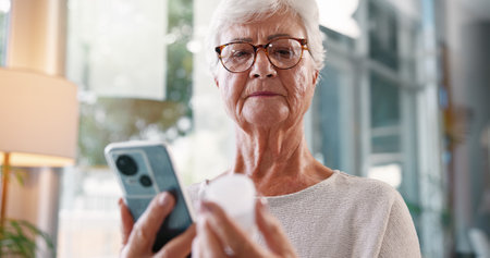 Elderly woman, research and medication with phone for telehealth, information or prescription at home. Senior, female person or patient with mobile smartphone or pills for symptoms or side effectsの写真素材