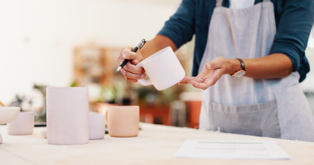 Workshop, hands and inspection with cup for pottery, small business and checklist for stock management. Closeup, person and potter with document for writing, order information and mug as productの写真素材