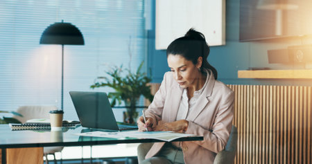 Business, woman and writing on document in office for notes, budget planning and schedule update. Female person, laptop and paperwork for reminder, information and audit checklist of financial reportの写真素材