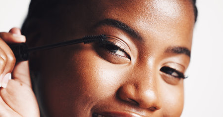 Mascara, portrait or black woman with beauty, makeup or skincare glow in studio on white background. Cosmetics brush, application or confident girl model with eyelash extensions for volume or lengthの写真素材