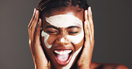 Excited, skincare and clay mask with black woman in studio for facial, spa results success or dermatology. Cosmetics, self care and pore cleaning benefits with person on dark background for happinessの写真素材