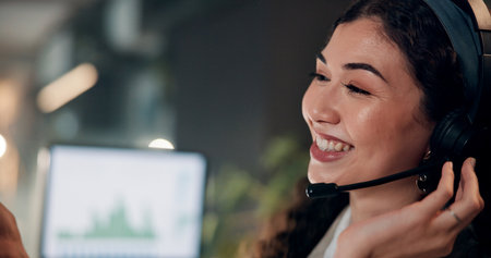 Headset, woman and tech support agent in office at night for crm, helpdesk or internet service provider. Happy, overtime and call center consultant with communication, consultation or contact us.の写真素材