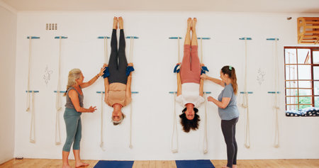 Stretching, upside down and rope on wall for yoga for senior group or people practice iyengar together in gym class. Women, body health and friends help for wellness, exercise and flexibility at clubの写真素材
