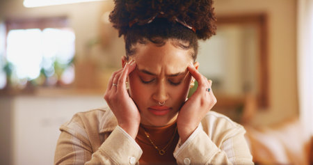 Headache, pain and face of woman in home for worry, stress and anxiety for student loans. Living room, house and person with migraine, burnout and fatigue for university debt, college funds or gradesの写真素材