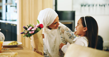Muslim, mother and child with flowers in home for mothers day surprise, birthday dinner and gratitude. Happy family, love and woman with bouquet gift at dining table for celebration and special eventの写真素材