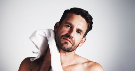 Portrait, man and towel for skincare in studio of cleaning, grooming routine and facial hair removal. Male person, drying face and fresh shave for hygiene care, beard maintenance and white backgroundの写真素材
