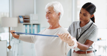 Senior woman, physiotherapist and resistance band with stretching, smile and healthcare services for recovery. People, happy and exercise with equipment, help and injury for rehabilitation at clinicの写真素材