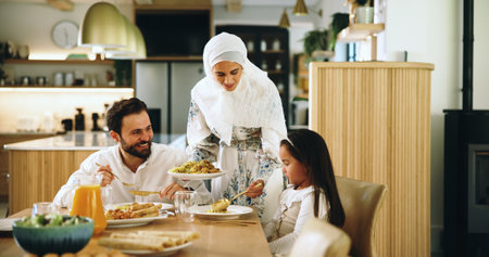 Muslim, parents and child with food at house for Eid lunch, healthy meal and feast for celebration. Mother, serving and family dish for nutrition, religious event and cuisine of Islamic cultureの写真素材