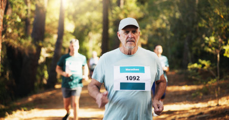 Competition, marathon and mature man in forest for challenge, performance or race. Cardio, fitness and running with athlete at outdoor event or rally in nature or woods for course, heat and trialの写真素材