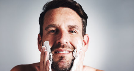 Man, portrait and shaving cream in studio with smile, grooming or hygiene with pride by background. Mature person, beard and foam for routine, self care or process for facial hair removal in Portugalの写真素材