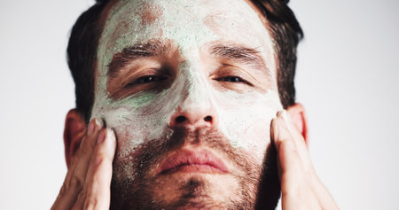 Facial, skincare and clay mask with portrait of man in studio for beauty, spa treatment and dermatology. Cosmetics, self care and pore cleaning benefits with person on white background for glowの写真素材